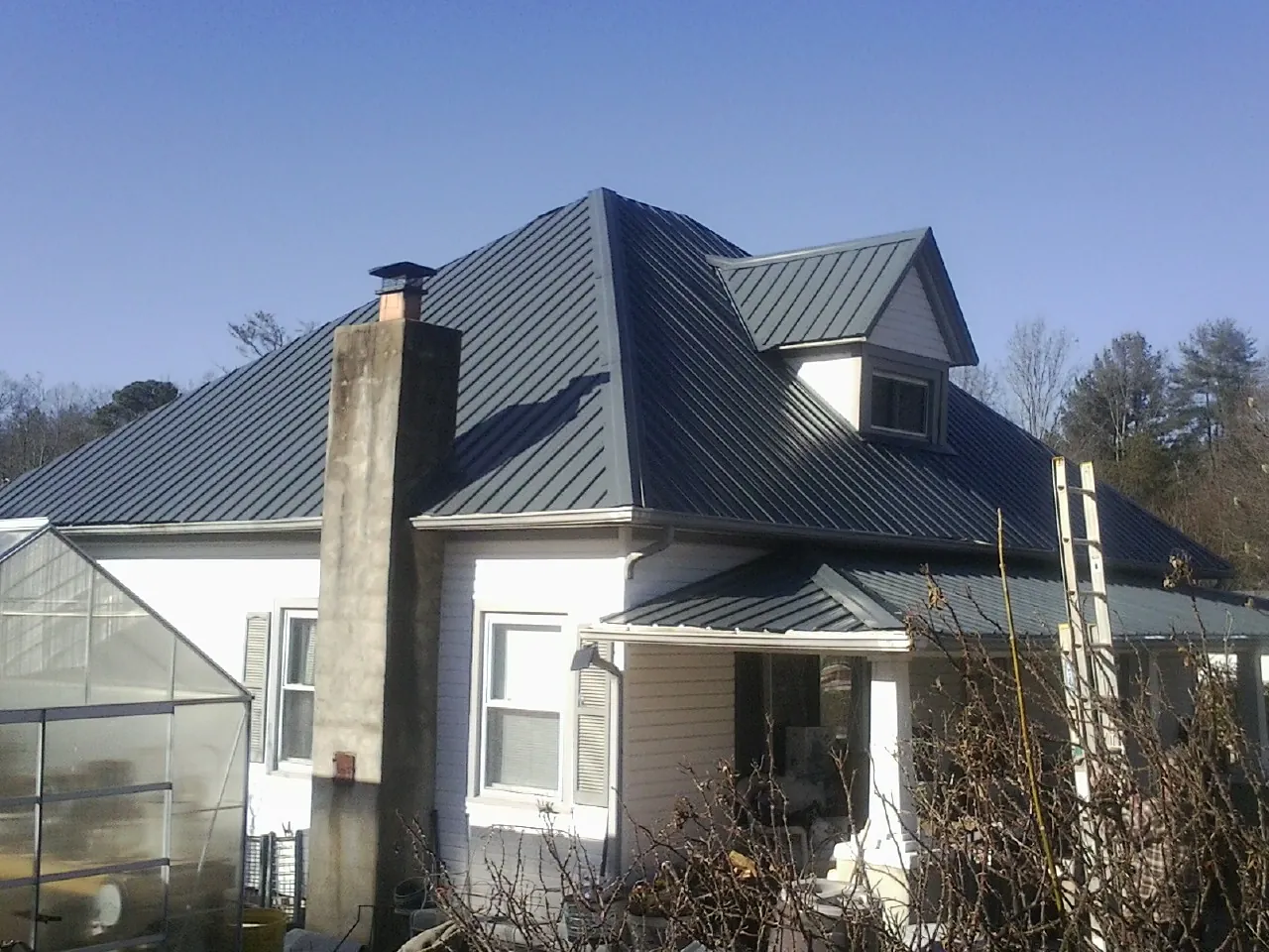 Dark blue standing seam metal roof on a white farmhouse with dormer — Slate & Tile Roof Repair by Roofing Brothers in Dunbarton