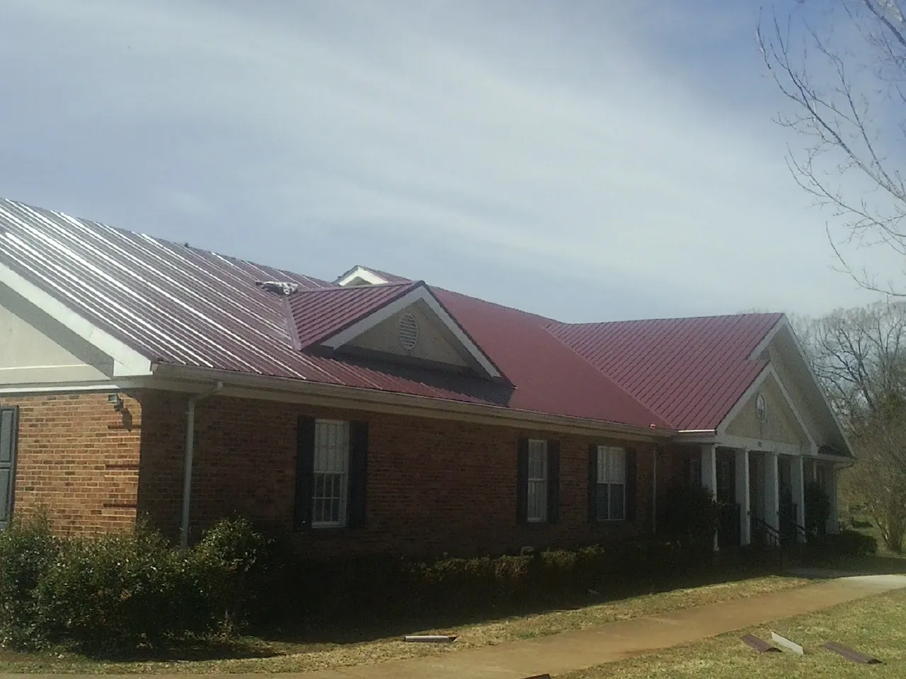 Red metal roof with gabled entries on a long brick building, from a Hail Damage Roof Repair job in Dunbarton