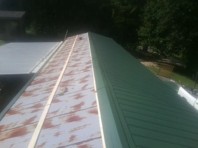 Old rusted panels beside newly installed green metal roofing — Wind Damage Roof Repair by Roofing Brothers in Dunbarton