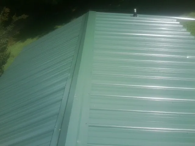 New green metal panels meeting at the ridge of a roof — Flat Roof Repair work by our crew in Dunbarton