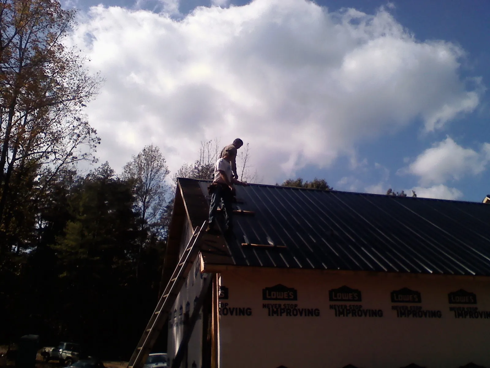 Roofer fastening dark metal panels high against a cloudy sky, from a Roof Inspection job in Dunbarton