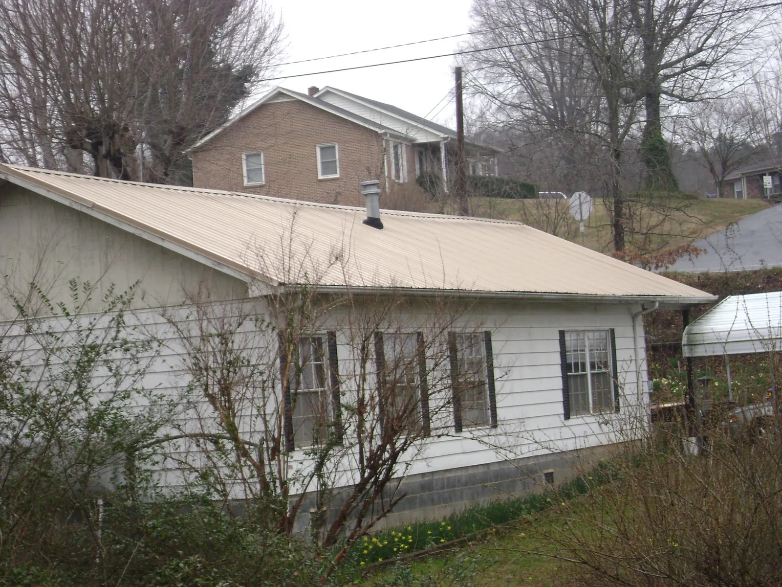 Tan metal roof on a white sided house set into a hillside — Commercial Roofing by Roofing Brothers in Dunbarton